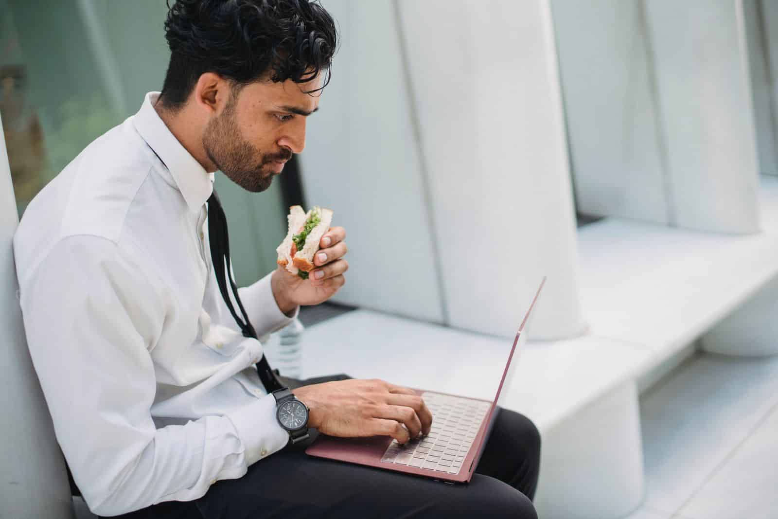 Businessman eating a quick lunch at his Businessman eating a quick lunch at his laptop during a busy workday